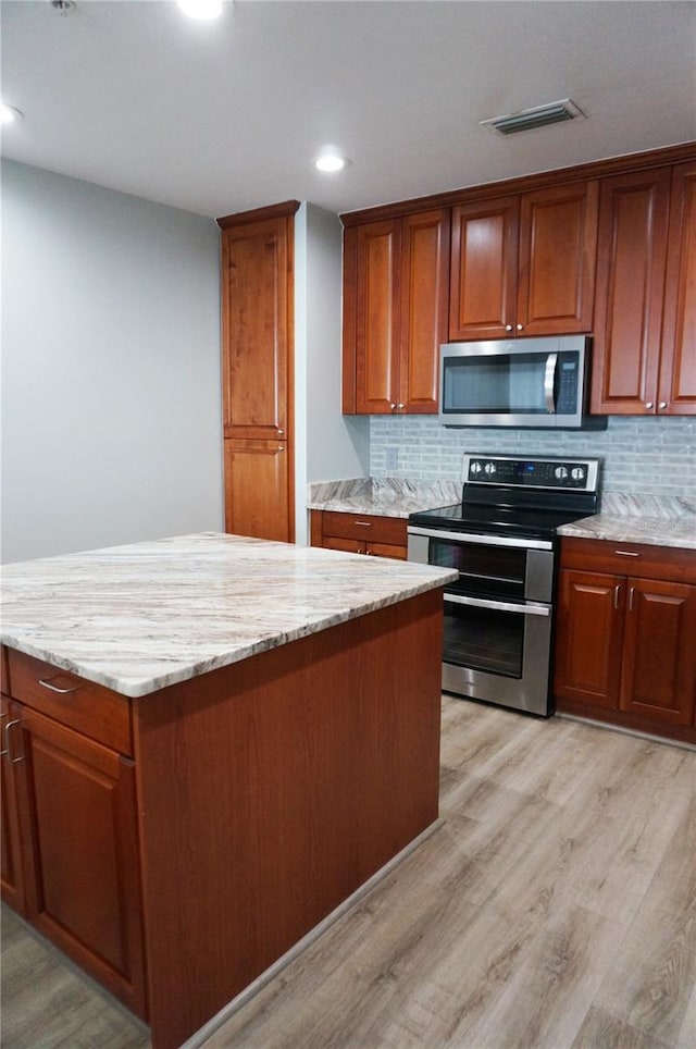 kitchen with tasteful backsplash, light stone countertops, stainless steel appliances, and light hardwood / wood-style floors