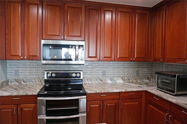 kitchen with tasteful backsplash, light stone counters, and appliances with stainless steel finishes