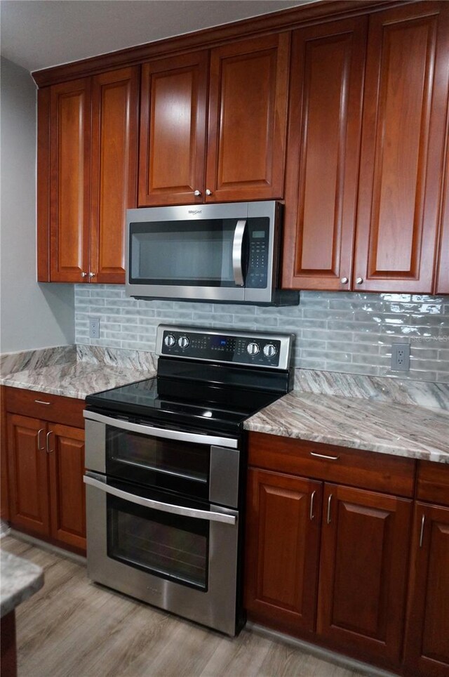 kitchen featuring light stone countertops, appliances with stainless steel finishes, light wood-type flooring, and decorative backsplash