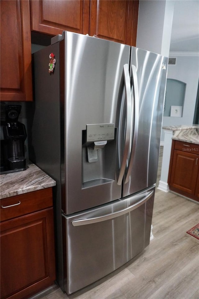 kitchen with stainless steel refrigerator with ice dispenser, light hardwood / wood-style floors, light stone counters, and crown molding