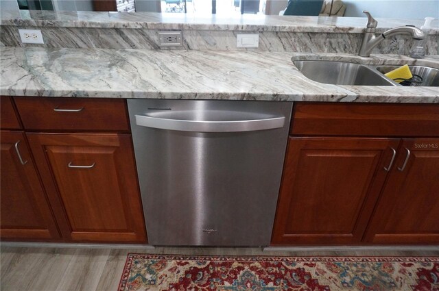 kitchen with stainless steel dishwasher, light stone counters, sink, and light hardwood / wood-style flooring