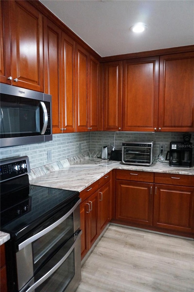 kitchen with light wood-type flooring, electric range, light stone counters, and backsplash