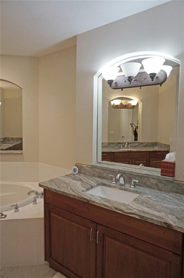 bathroom featuring tile patterned floors, a relaxing tiled tub, and vanity