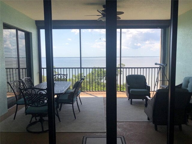 sunroom with ceiling fan and a water view