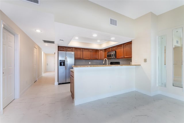 kitchen with kitchen peninsula, appliances with stainless steel finishes, tasteful backsplash, a tray ceiling, and sink