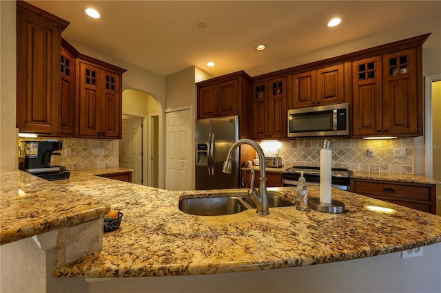 kitchen featuring kitchen peninsula, appliances with stainless steel finishes, light stone countertops, and sink