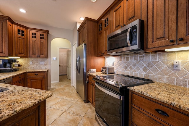 kitchen featuring light stone countertops, appliances with stainless steel finishes, tasteful backsplash, and light tile patterned flooring