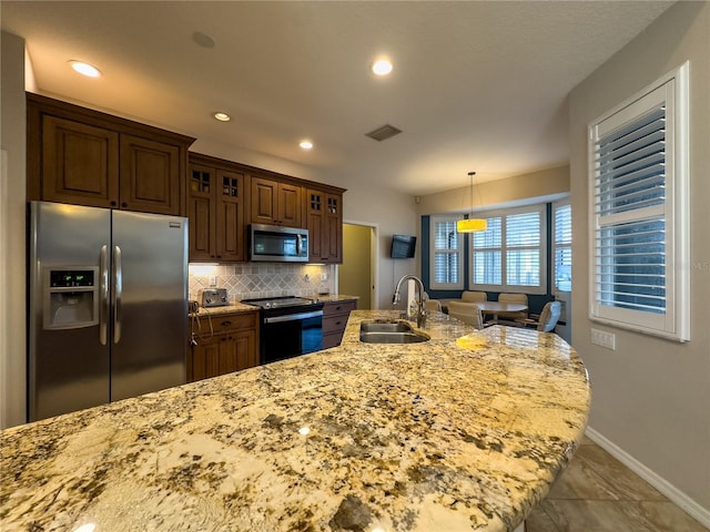 kitchen with pendant lighting, sink, appliances with stainless steel finishes, tasteful backsplash, and light stone counters