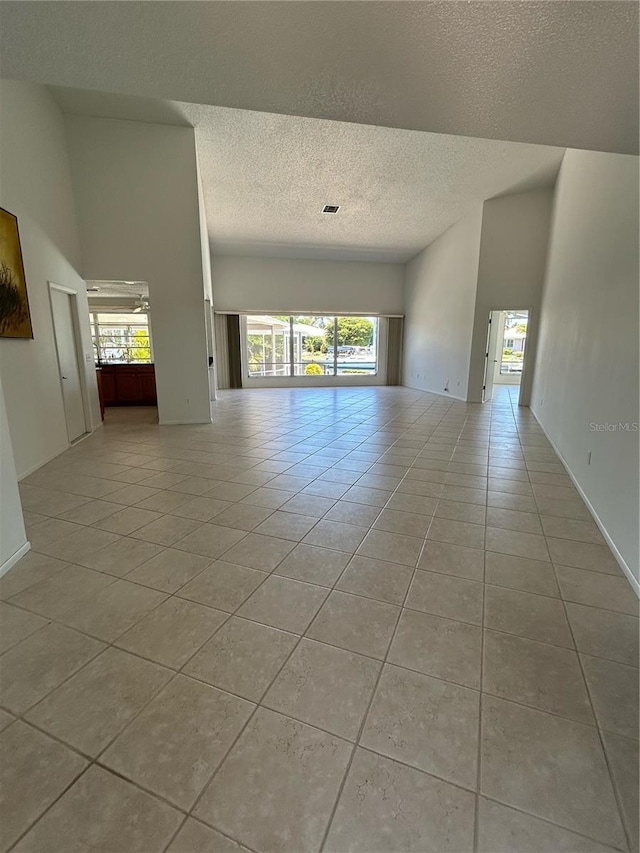 tiled empty room with a textured ceiling and a high ceiling