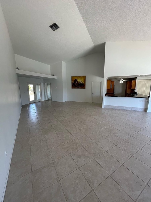 unfurnished living room featuring ceiling fan, french doors, a textured ceiling, vaulted ceiling, and light tile patterned floors