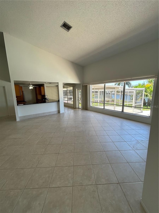 unfurnished living room with ceiling fan, a towering ceiling, light tile patterned flooring, and a textured ceiling