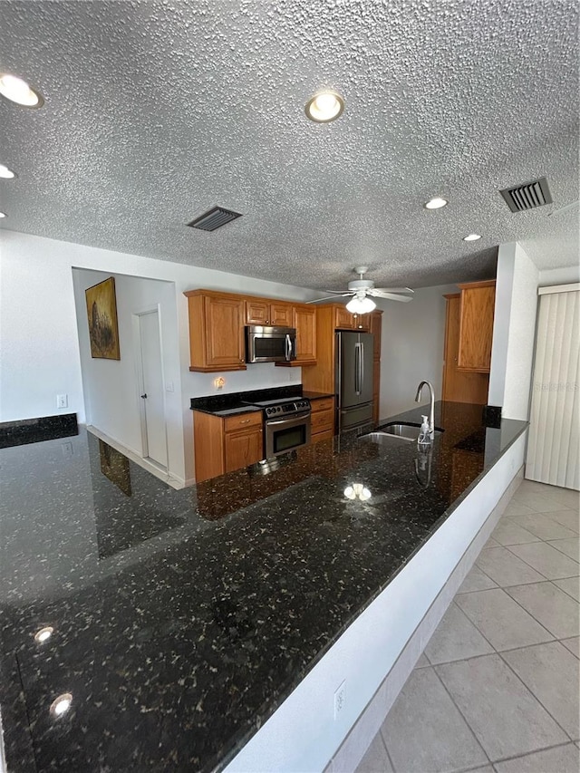 kitchen featuring sink, kitchen peninsula, dark stone countertops, light tile patterned floors, and appliances with stainless steel finishes