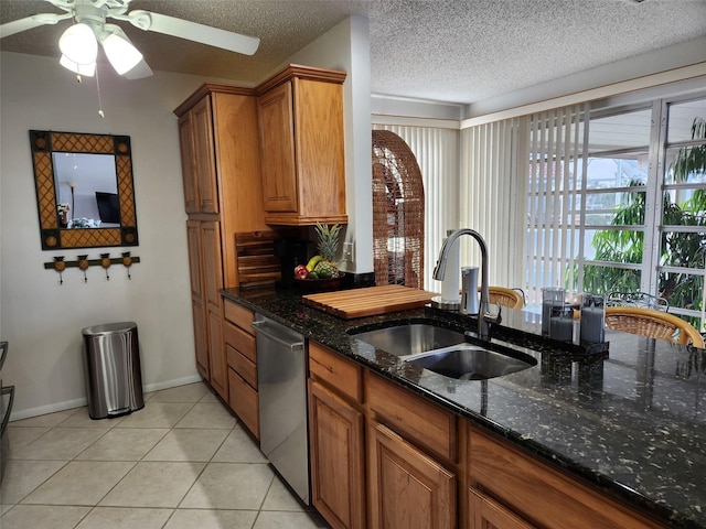 kitchen with stainless steel dishwasher, dark stone counters, a textured ceiling, sink, and light tile patterned flooring