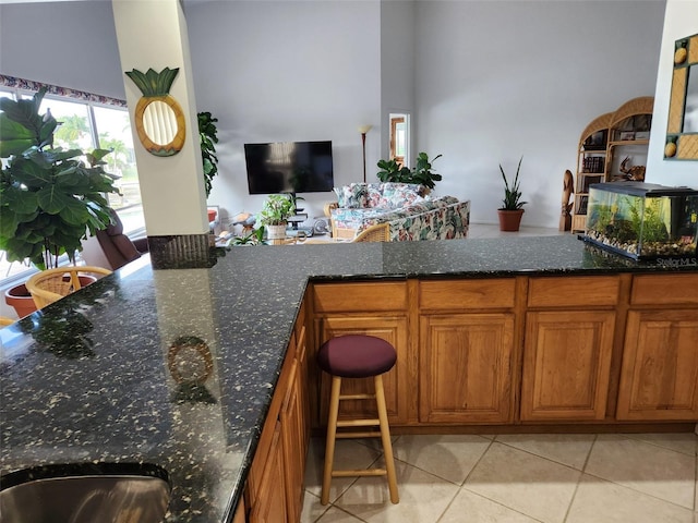 kitchen featuring light tile patterned flooring, dark stone countertops, and a breakfast bar area