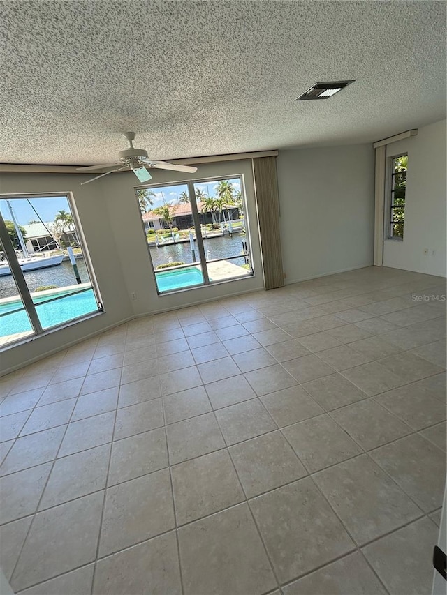 tiled empty room with ceiling fan, a water view, and a textured ceiling