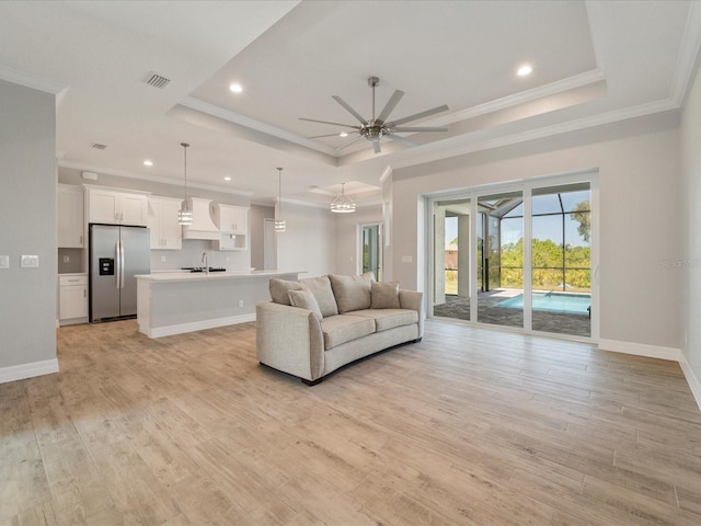 unfurnished living room with ornamental molding, ceiling fan, light hardwood / wood-style floors, and a raised ceiling