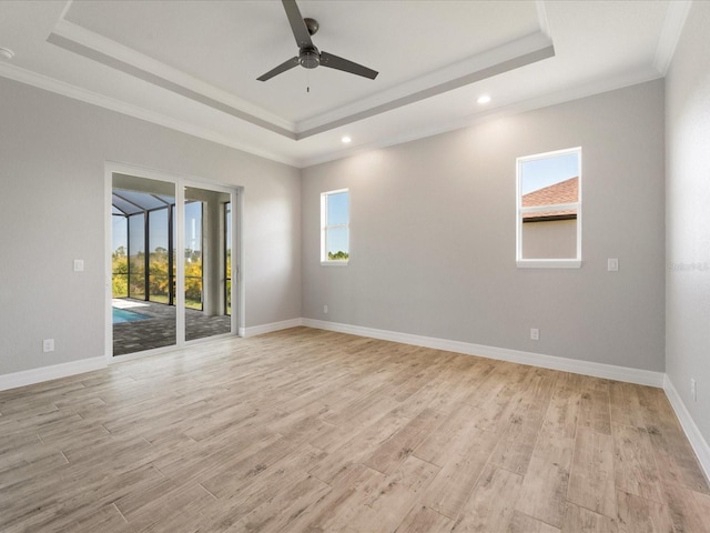 spare room with a tray ceiling, crown molding, ceiling fan, and light hardwood / wood-style flooring