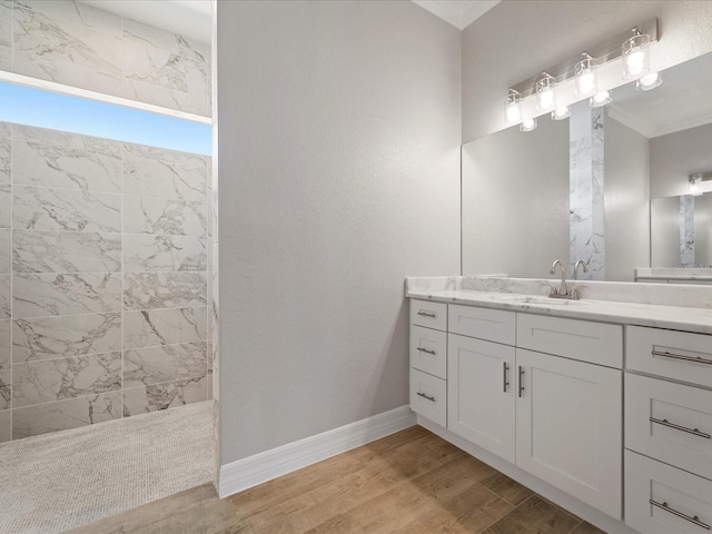 bathroom with a tile shower, vanity, hardwood / wood-style flooring, and ornamental molding