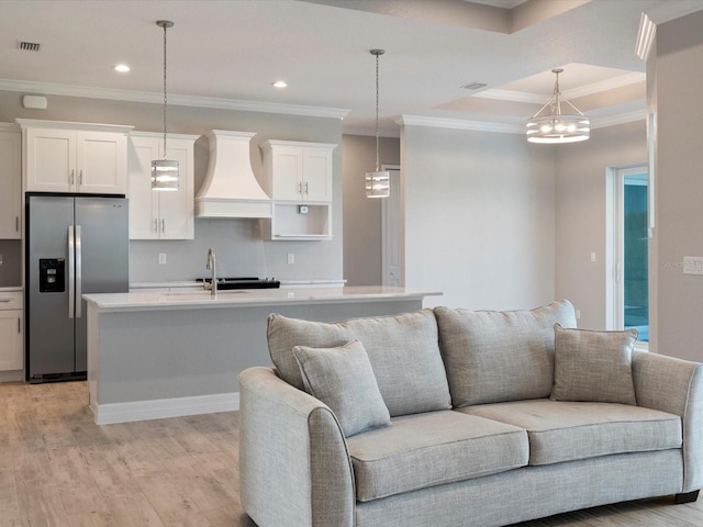 kitchen with a kitchen island with sink, light wood-type flooring, premium range hood, and stainless steel fridge