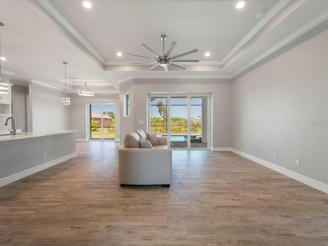 unfurnished living room featuring sink, ornamental molding, ceiling fan, a raised ceiling, and light wood-type flooring