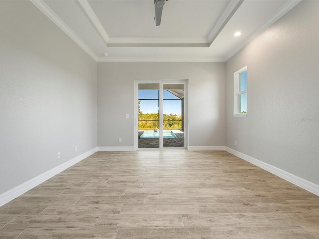 empty room with ceiling fan, a tray ceiling, light hardwood / wood-style floors, and crown molding