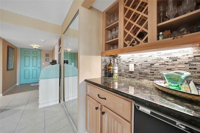 bar with light brown cabinets, backsplash, dark stone countertops, light tile patterned floors, and black dishwasher