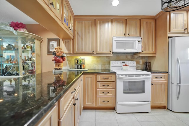 kitchen with tasteful backsplash, light tile patterned flooring, dark stone counters, and white appliances