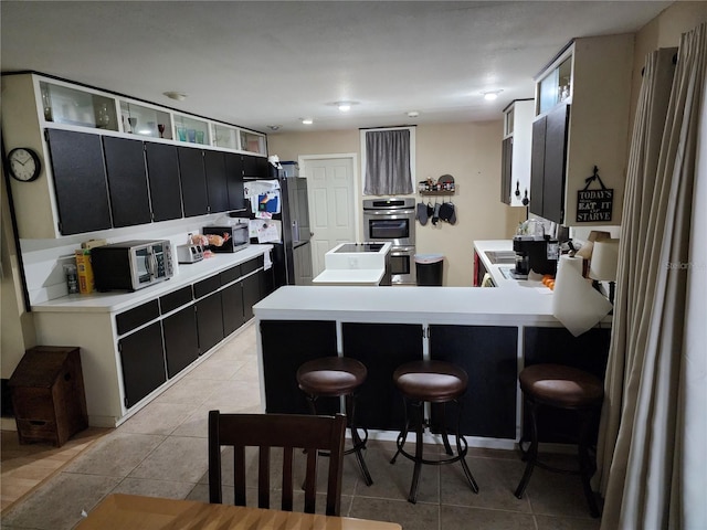 kitchen featuring light tile patterned floors, a breakfast bar, appliances with stainless steel finishes, and kitchen peninsula