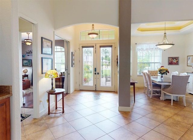 entryway featuring french doors, ceiling fan, light tile patterned floors, ornamental molding, and a tray ceiling