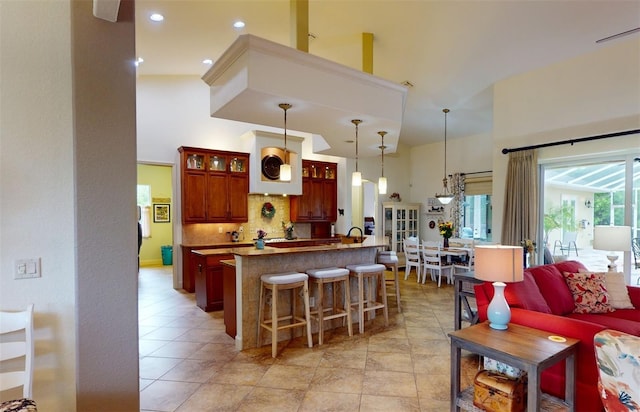 kitchen featuring hanging light fixtures, a towering ceiling, tasteful backsplash, light tile patterned flooring, and a breakfast bar area