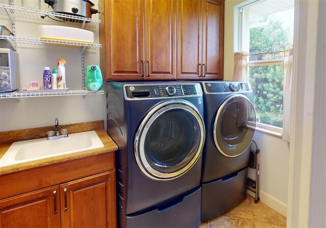 clothes washing area with washing machine and clothes dryer, sink, light tile patterned floors, and cabinets