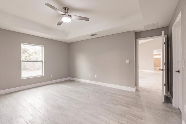 unfurnished room with light wood-type flooring, a raised ceiling, and ceiling fan