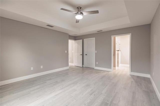 unfurnished bedroom with light hardwood / wood-style floors, a raised ceiling, and ceiling fan