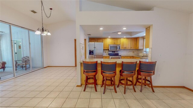 kitchen with kitchen peninsula, a kitchen bar, stainless steel appliances, vaulted ceiling, and an inviting chandelier