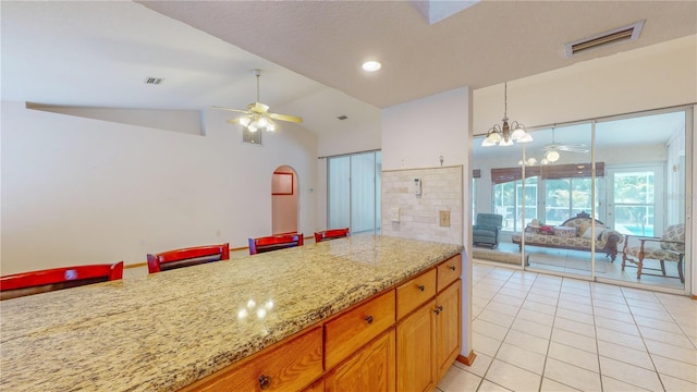 kitchen with light stone countertops, ceiling fan with notable chandelier, light tile patterned floors, decorative light fixtures, and lofted ceiling