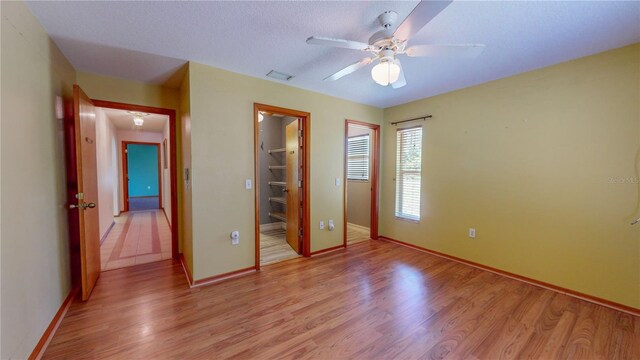 unfurnished bedroom with ceiling fan, light hardwood / wood-style floors, a spacious closet, and a closet