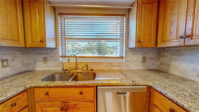 kitchen with stainless steel dishwasher, decorative backsplash, sink, and light stone countertops