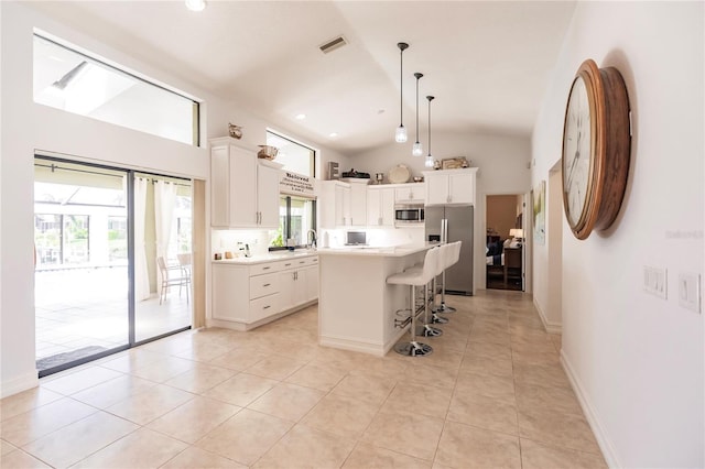 kitchen with a kitchen island, vaulted ceiling, decorative light fixtures, light tile patterned floors, and appliances with stainless steel finishes