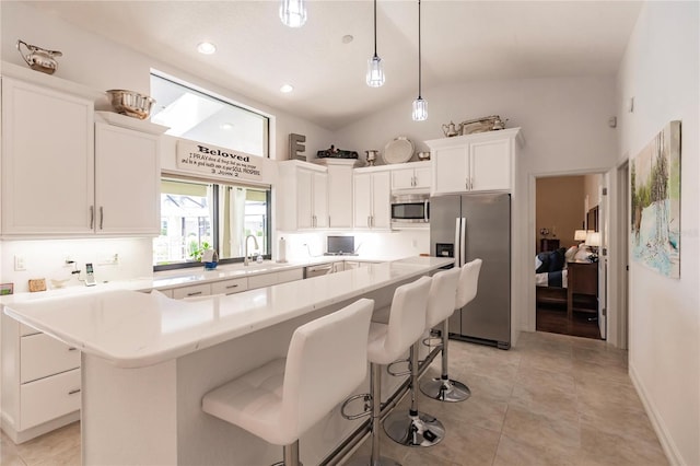 kitchen featuring vaulted ceiling, decorative light fixtures, a kitchen island, white cabinetry, and stainless steel appliances