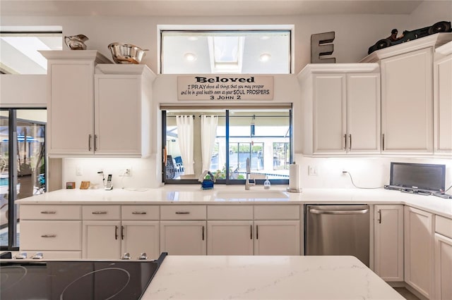 kitchen with stainless steel dishwasher, light stone counters, white cabinets, and sink