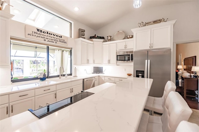 kitchen featuring white cabinets, a kitchen breakfast bar, sink, vaulted ceiling, and stainless steel appliances