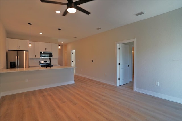 interior space featuring stainless steel appliances, backsplash, light wood-type flooring, pendant lighting, and white cabinets