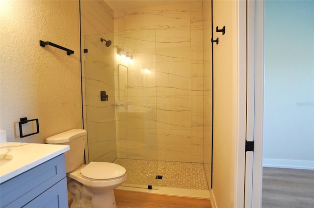 bathroom with hardwood / wood-style flooring, toilet, vanity, and a tile shower