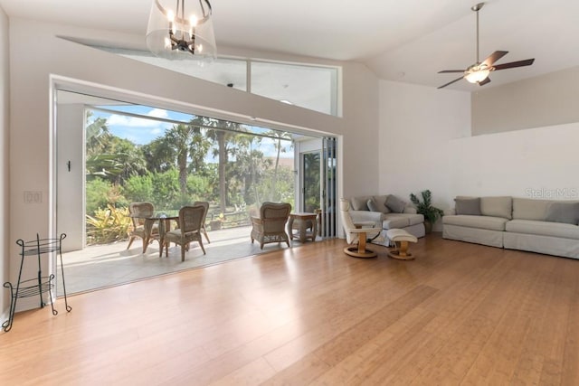 living room featuring ceiling fan with notable chandelier, light wood-type flooring, and vaulted ceiling