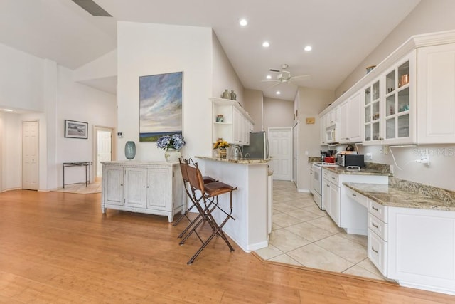 kitchen featuring a breakfast bar, white appliances, white cabinets, light stone counters, and kitchen peninsula