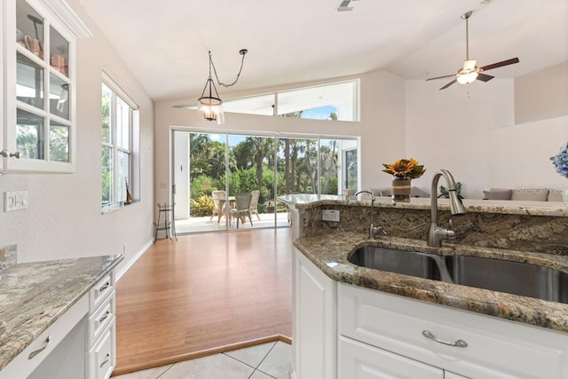 kitchen with white cabinets, sink, vaulted ceiling, dark stone countertops, and light tile patterned floors