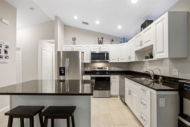 kitchen with appliances with stainless steel finishes, vaulted ceiling, sink, a center island, and white cabinetry