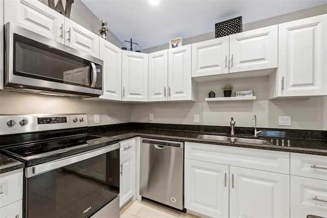 kitchen featuring dark stone counters, white cabinets, sink, light tile patterned floors, and appliances with stainless steel finishes