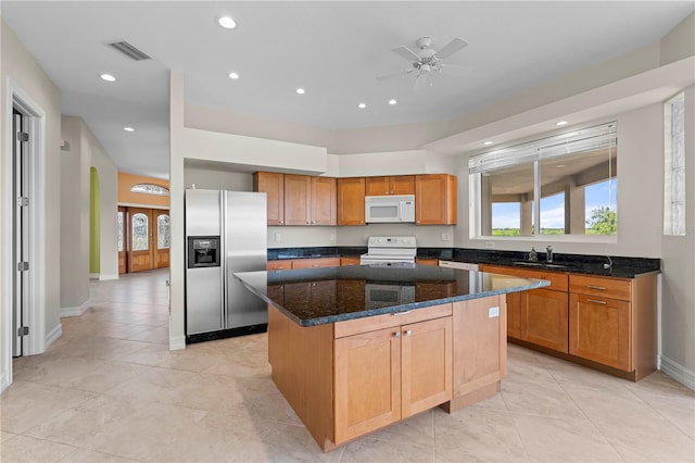 kitchen with ceiling fan, a kitchen island, dark stone countertops, white appliances, and light tile patterned floors