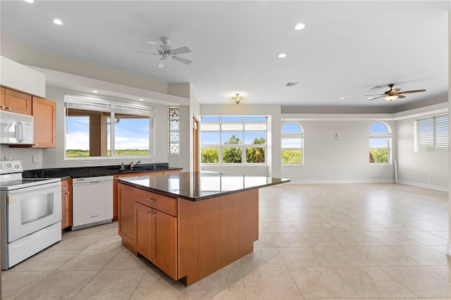 kitchen with ceiling fan, a center island, dark stone countertops, white appliances, and light tile patterned flooring